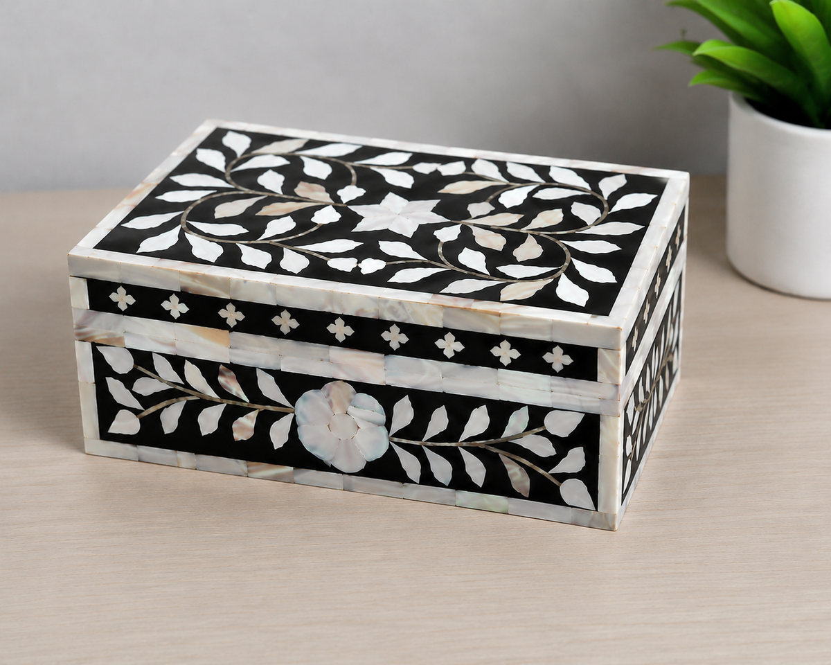 Black mother of pearl jewelry box styled with decorative accessories on a tabletop.